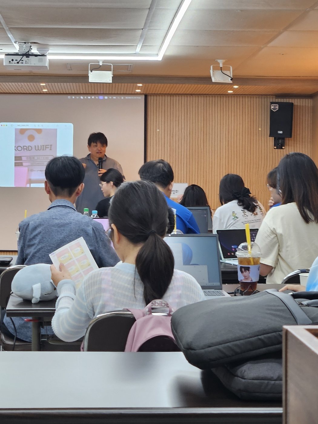 END NF AI 교육 강의 장면 — 강사가 마이크를 들고 설명하고 참가자들이 노트북 앞에 앉아 있는 모습